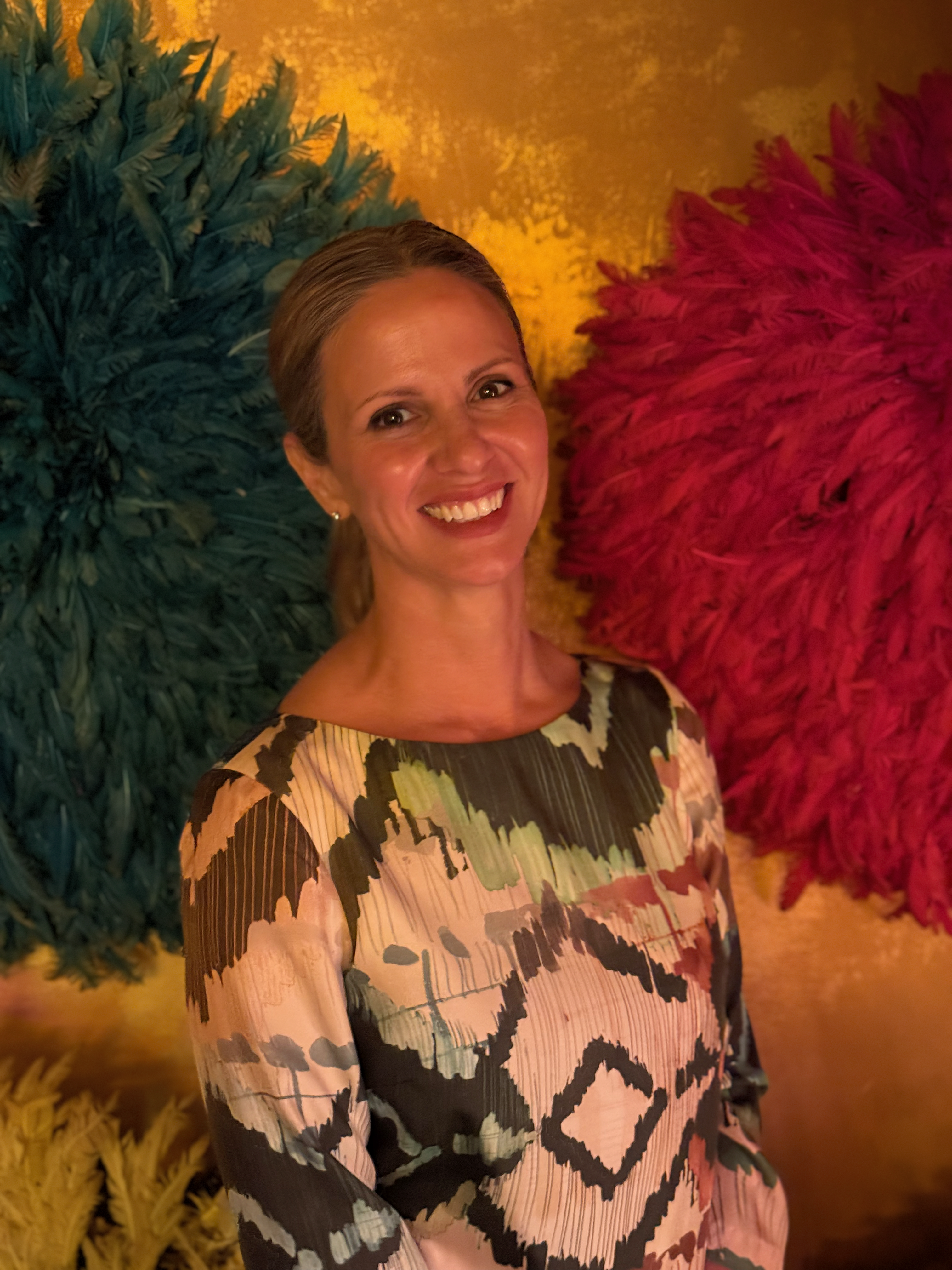 Rebecca smiling between teal and burgundy feathered decorations